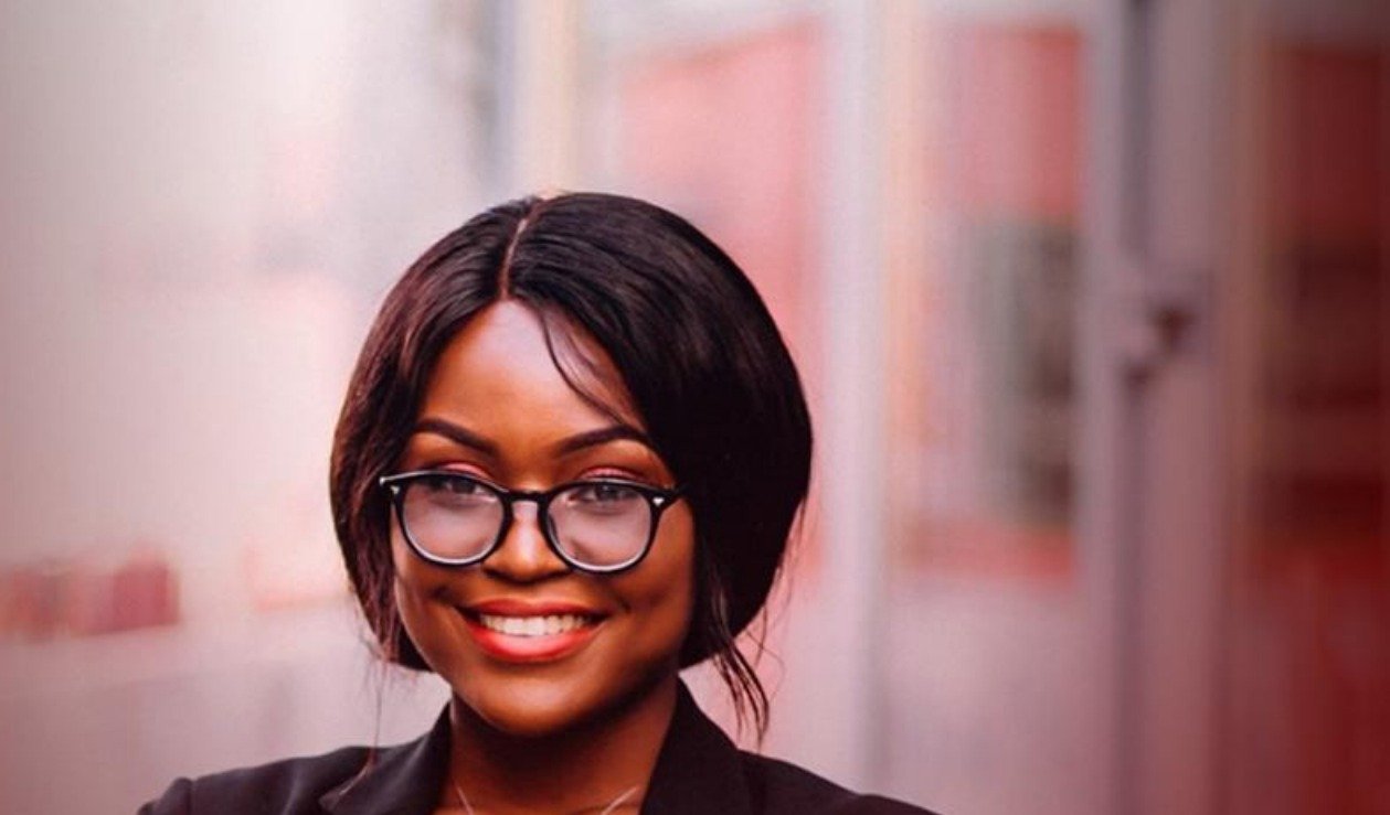 Mulher empreendedora de blazer preto e óculos, de braços cruzados, sorrindo